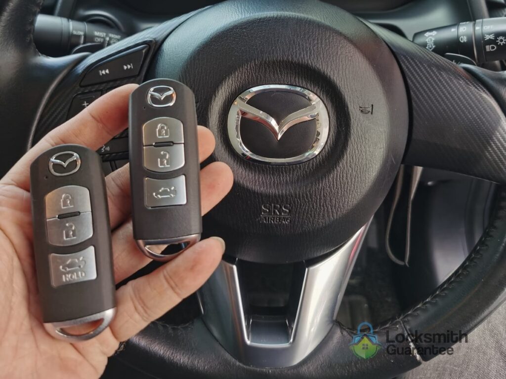 Hand holding car keys in front of a Mazda steering wheel.