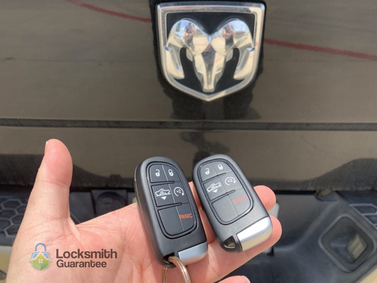 Hand holding car key fobs in front of vehicle emblem.