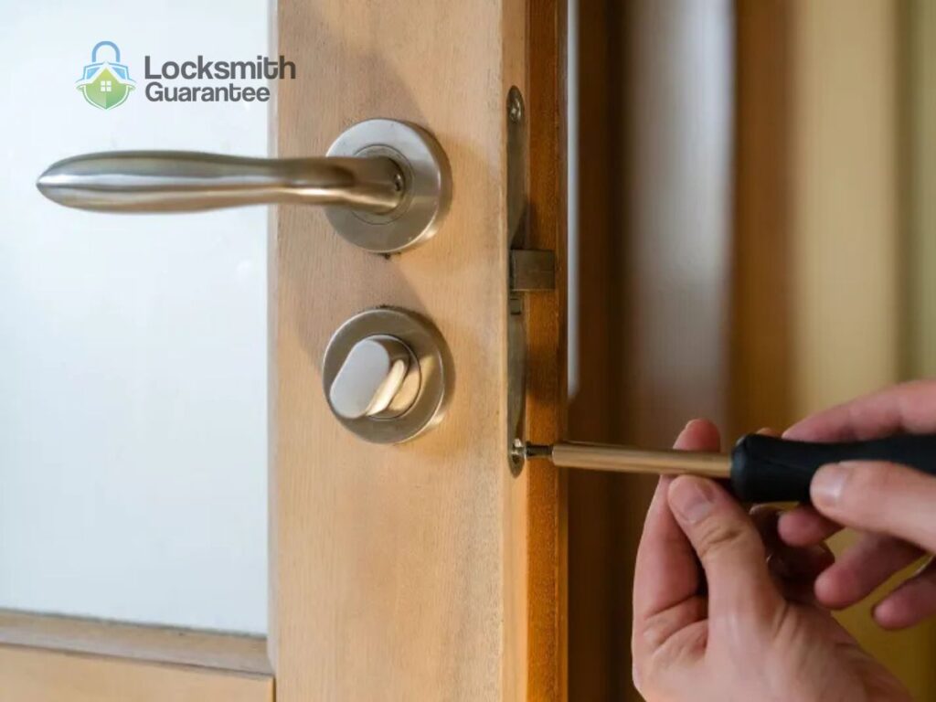 Person repairing door lock with screwdriver indoors.